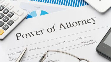 Power of Attorney form on desk strewn with glasses, pen, calculator, statement, phone and iPad