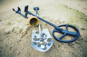 Metal detector on beach with shovel, jar, and coins
